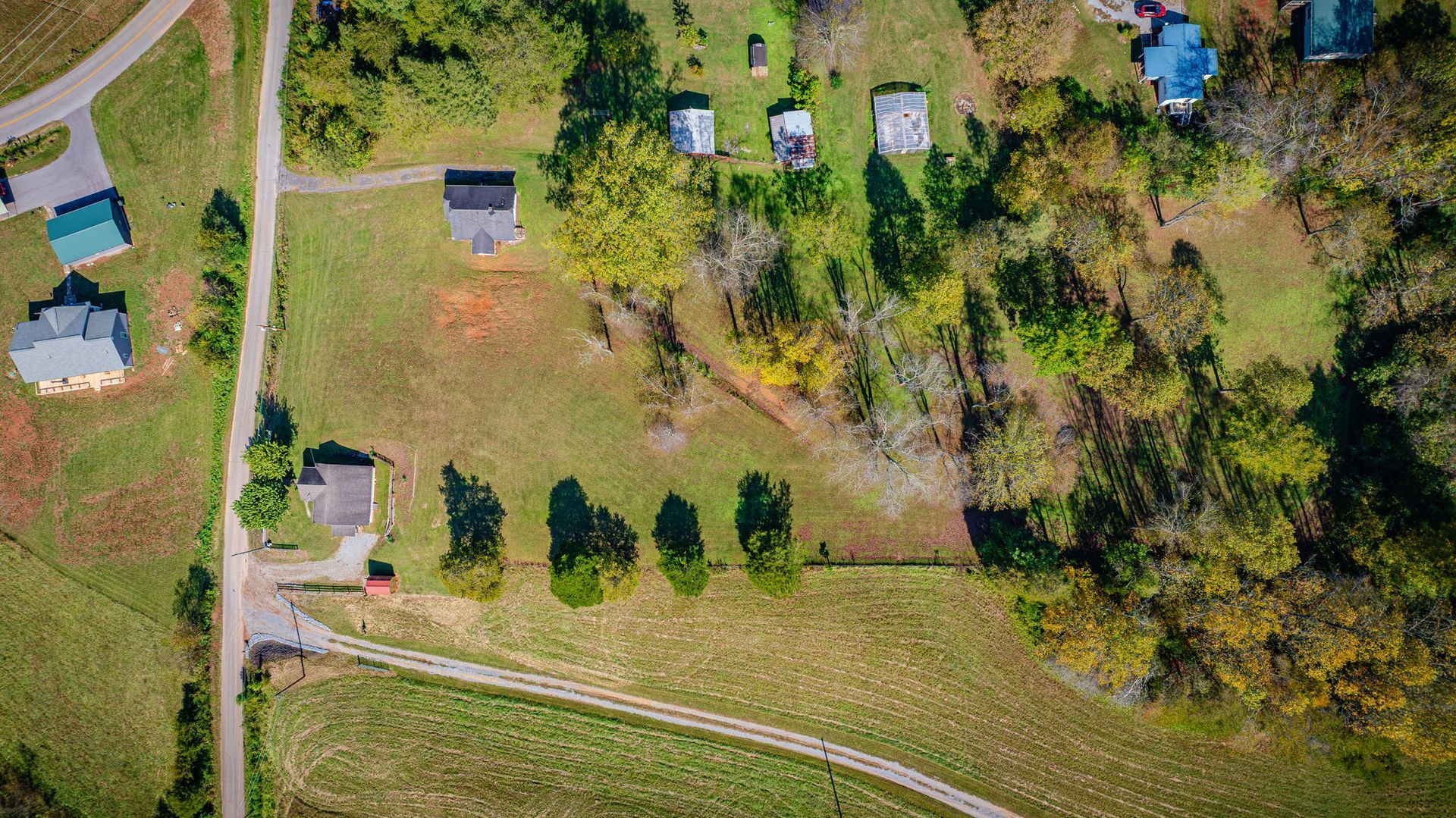 Aerial view of rural homes, trees, and grassy fields along a curving road