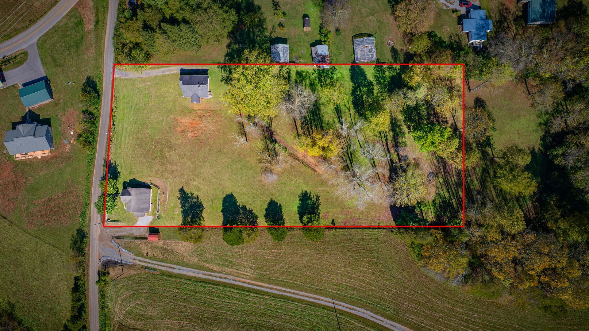 Aerial view of a grassy property outlined in red beside a road and trees, with a small building and parked vehicles