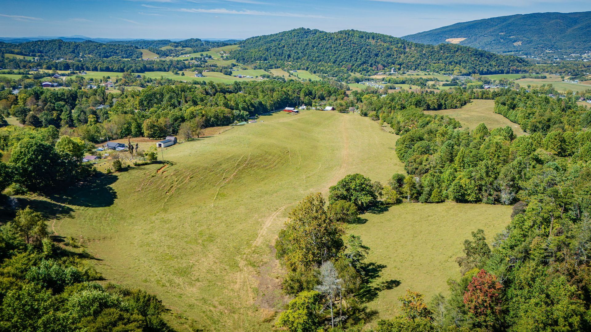 Green hillside meadow surrounded by dense trees, with rolling hills and mountains in the distance.