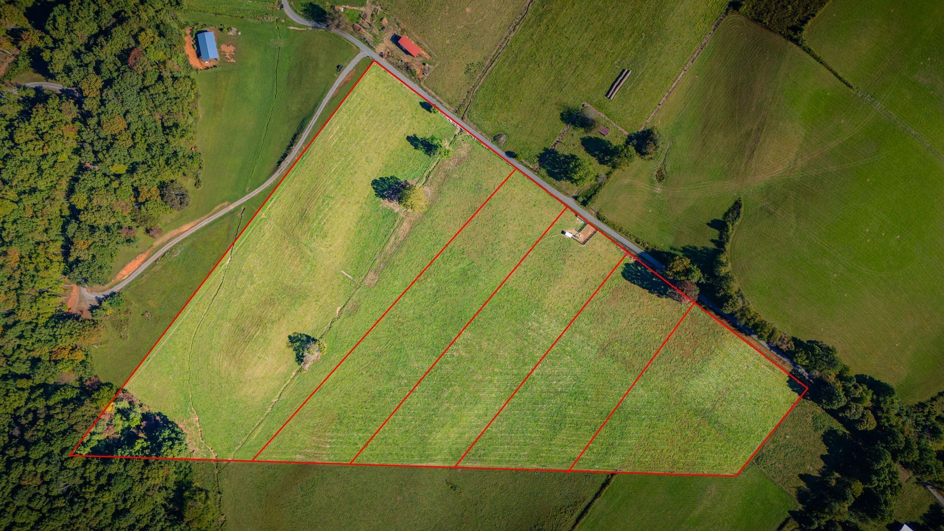 Aerial view of a grassy field bordered by trees, marked with red diagonal lines and a small blue structure.