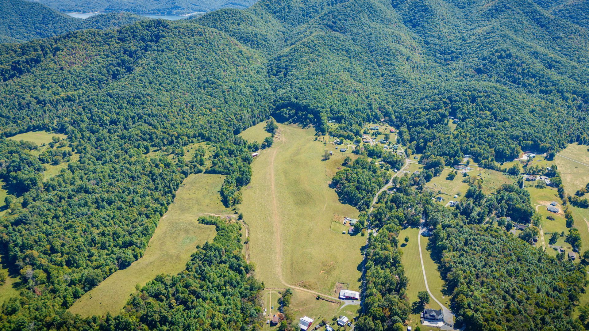 Aerial view of a grassy airstrip cutting through dense green forest and hills