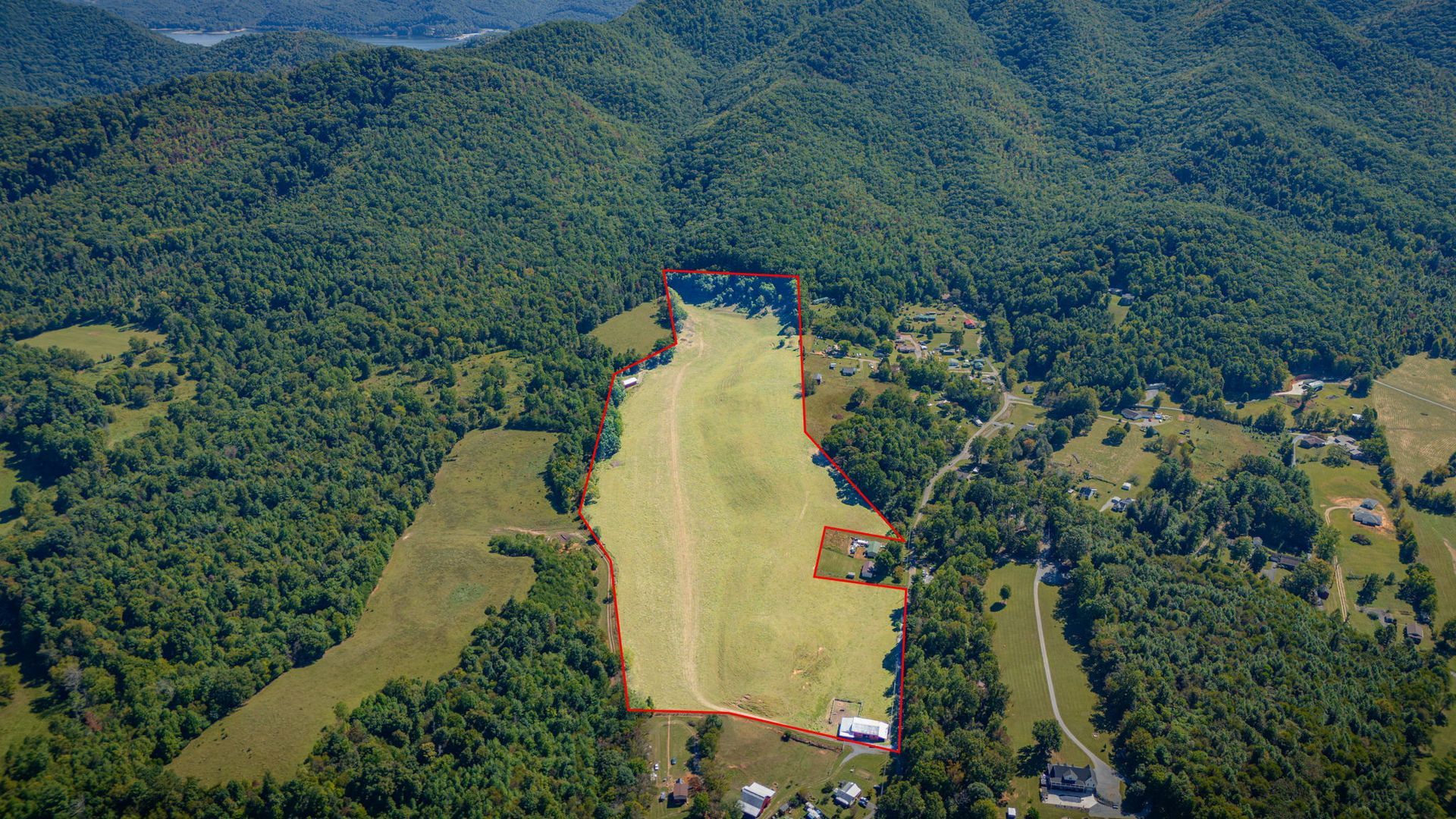 Aerial view of a large grassy field cleared in a dense green forest, with a few tents or structures at the edge.