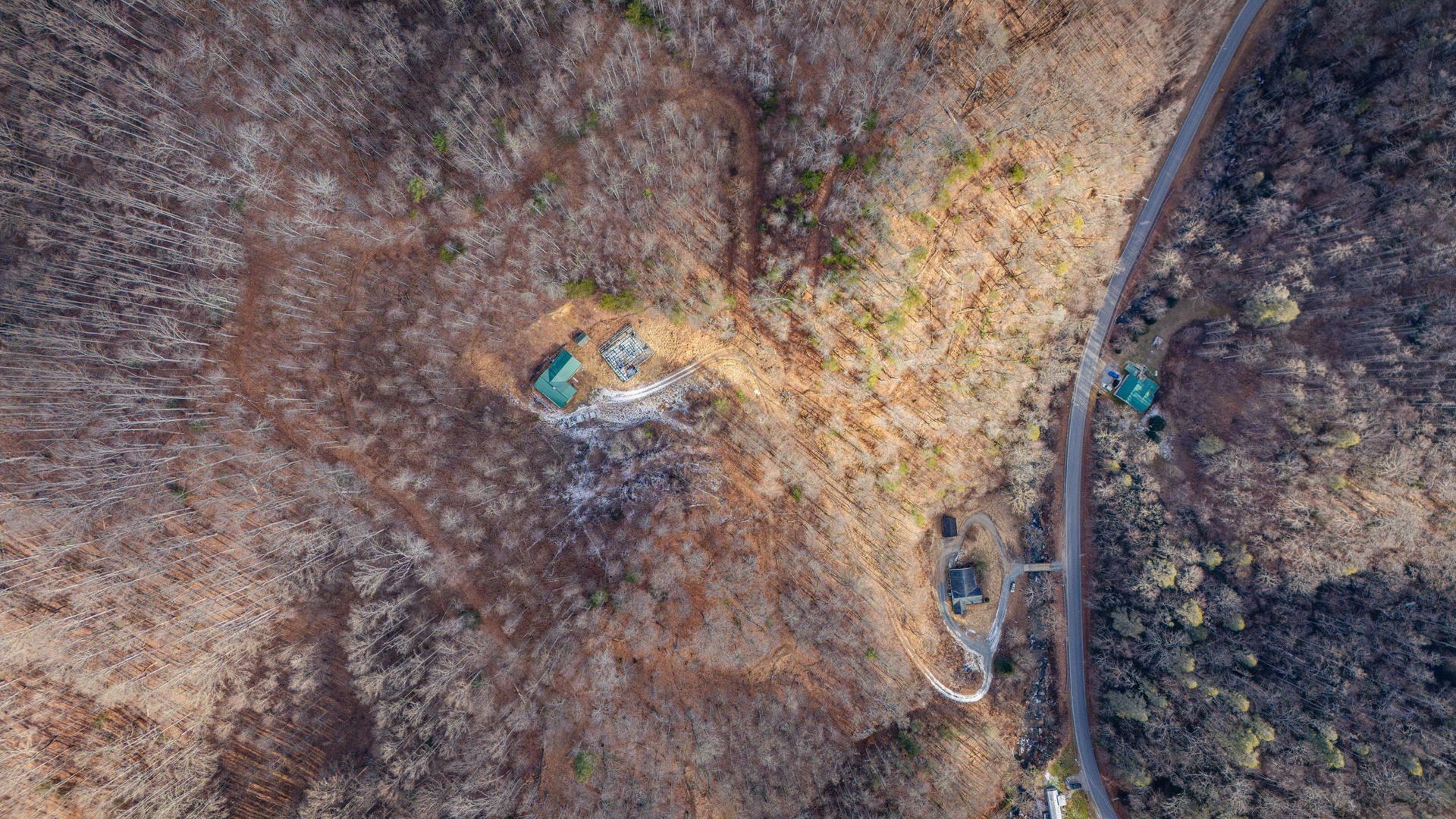 Overhead view of a mountain landscape with trees, road, and small structures.