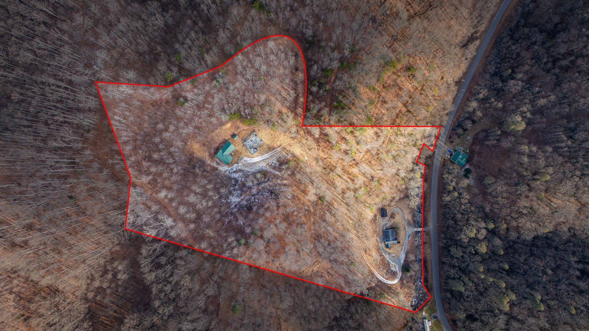 Aerial view of a wooded lot outlined in red, with a road and a few structures visible.