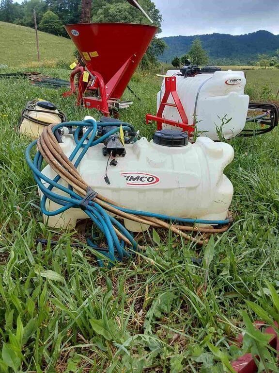 Farm sprayer with red hopper, white tank, and blue hoses in a grassy field