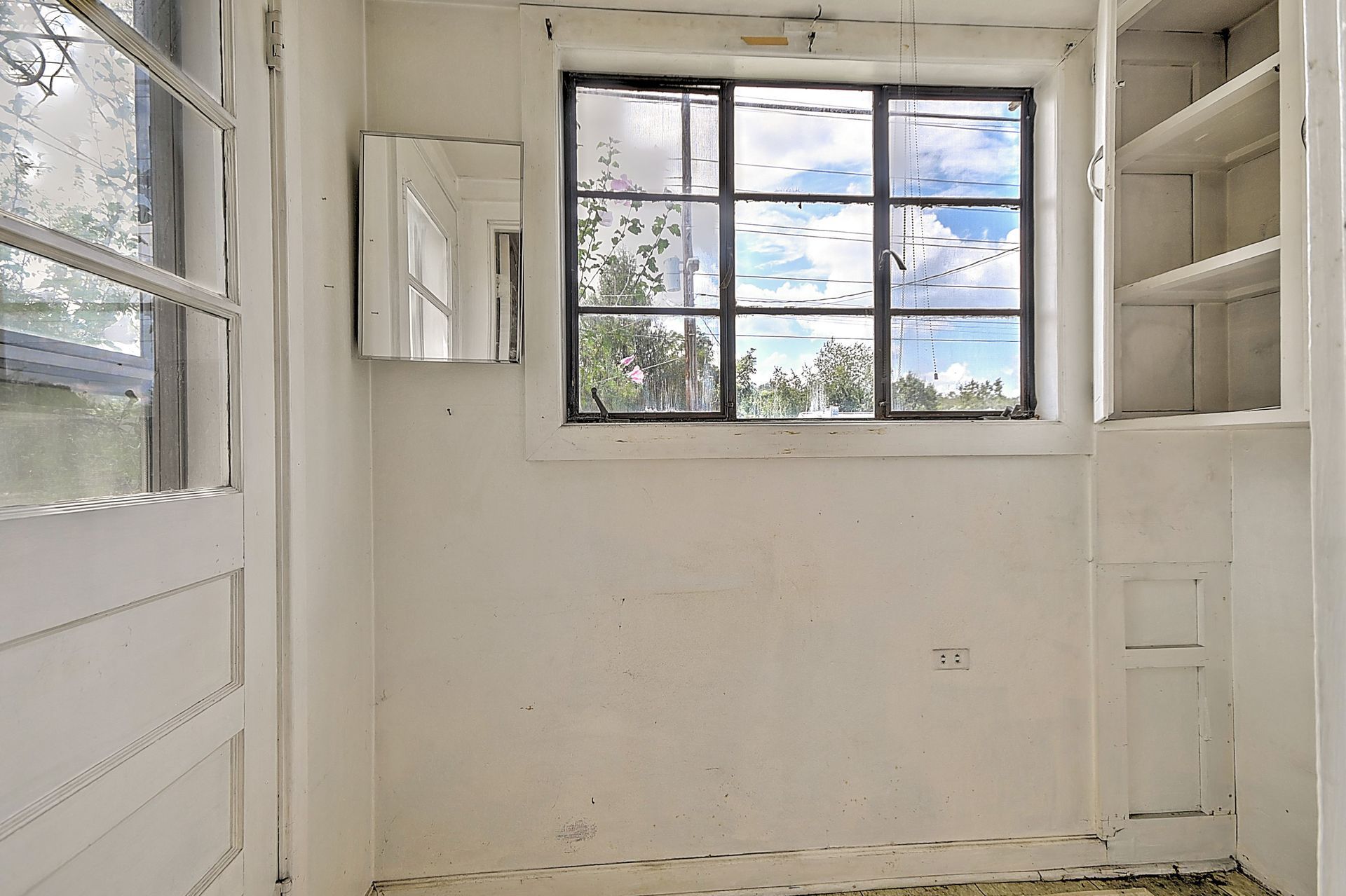 Empty white room with window, built-in shelves, and open door, lit by daylight