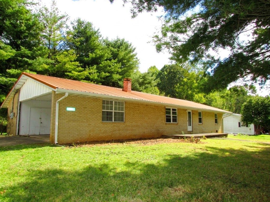 Single-story brick house with red roof and white carport, surrounded by green lawn and trees