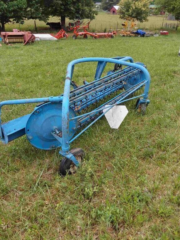 Blue farm implement with rotating reel sitting in a grassy field