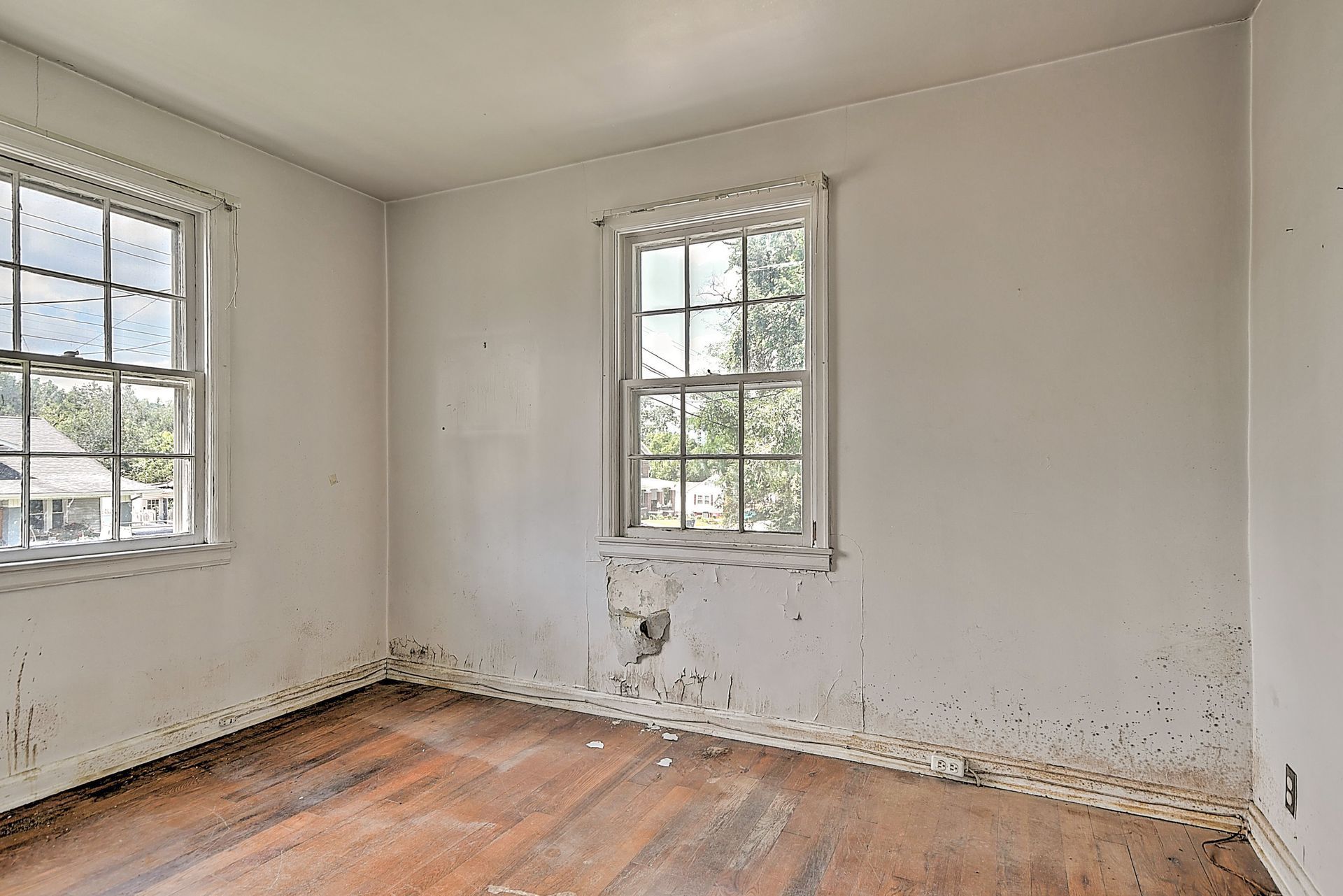 Empty white room with two windows, peeling paint, and a worn wooden floor.