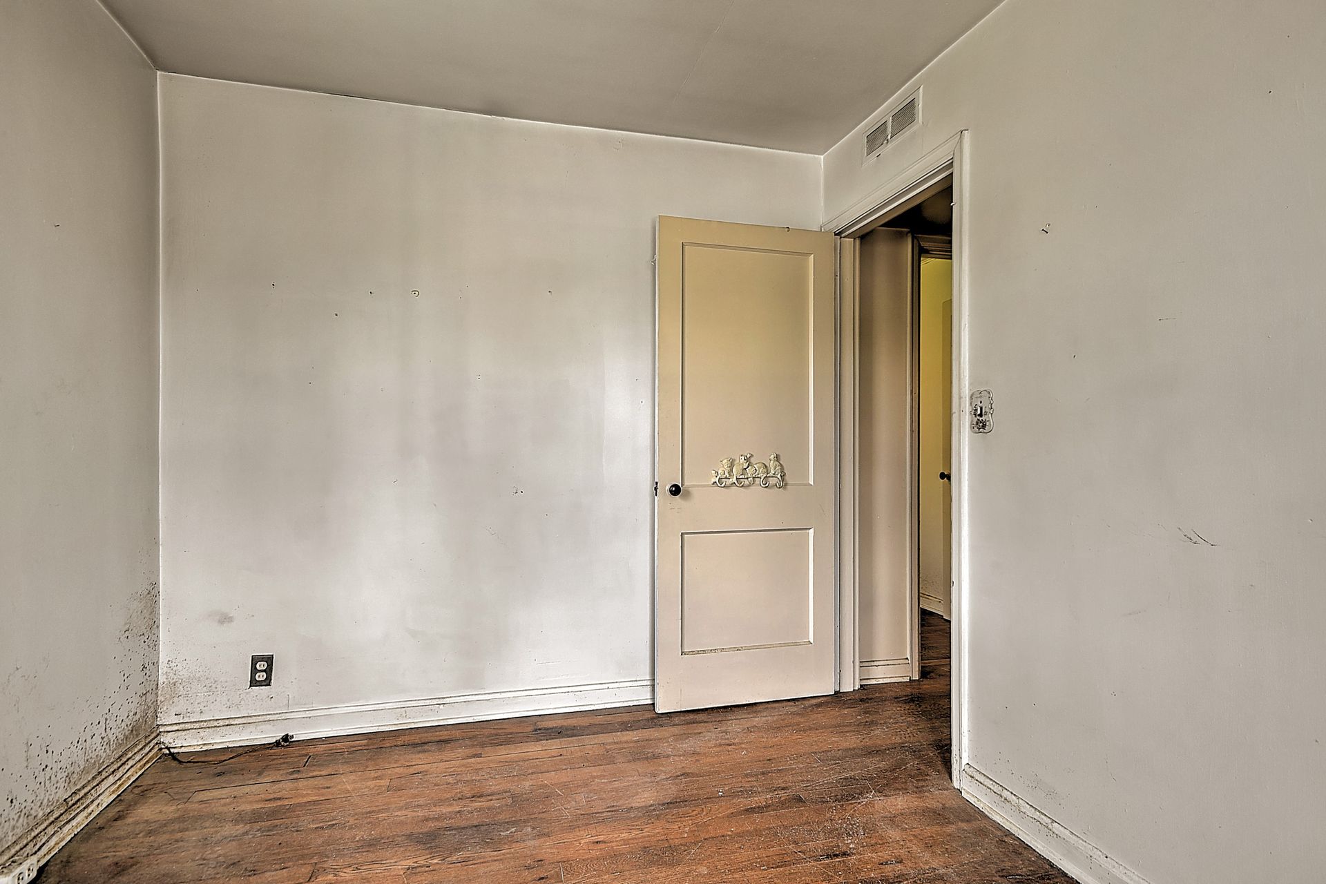 Empty room with worn wood floor, white walls, and an open door to a hallway.