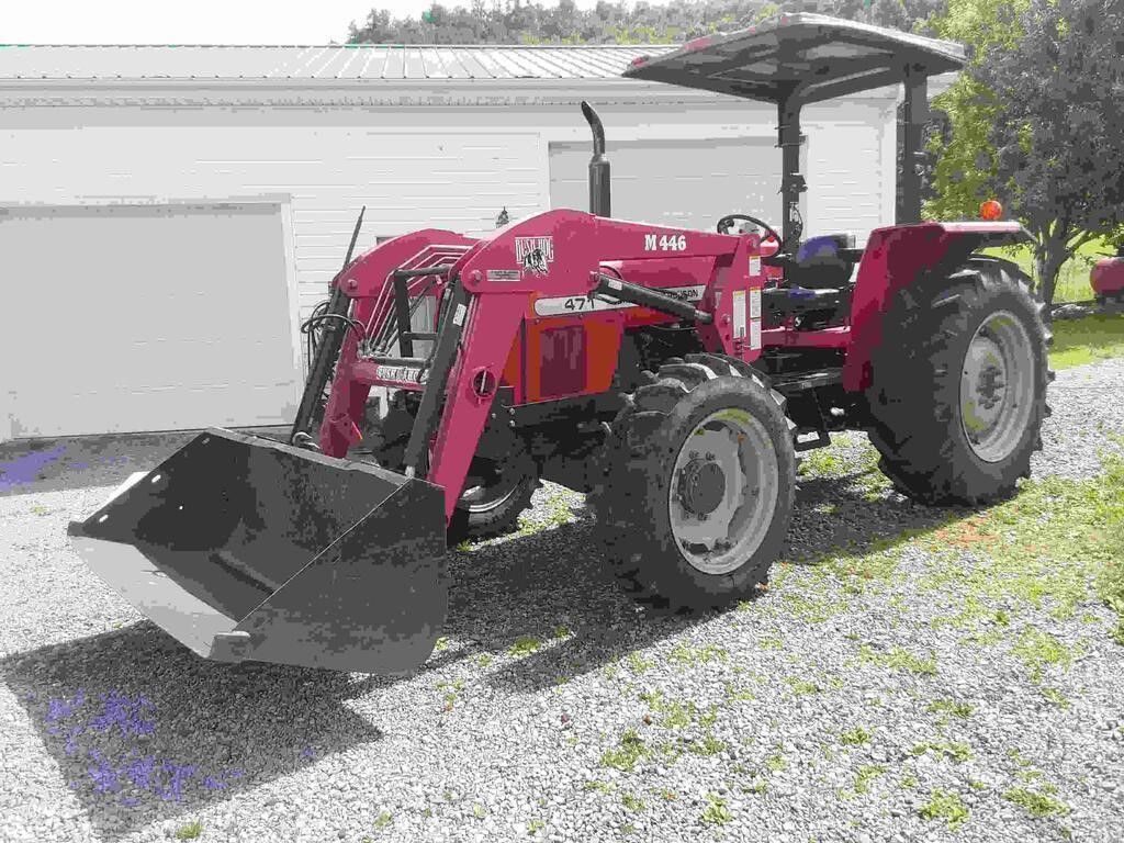 Red tractor with front loader parked on gravel beside a garage and field.