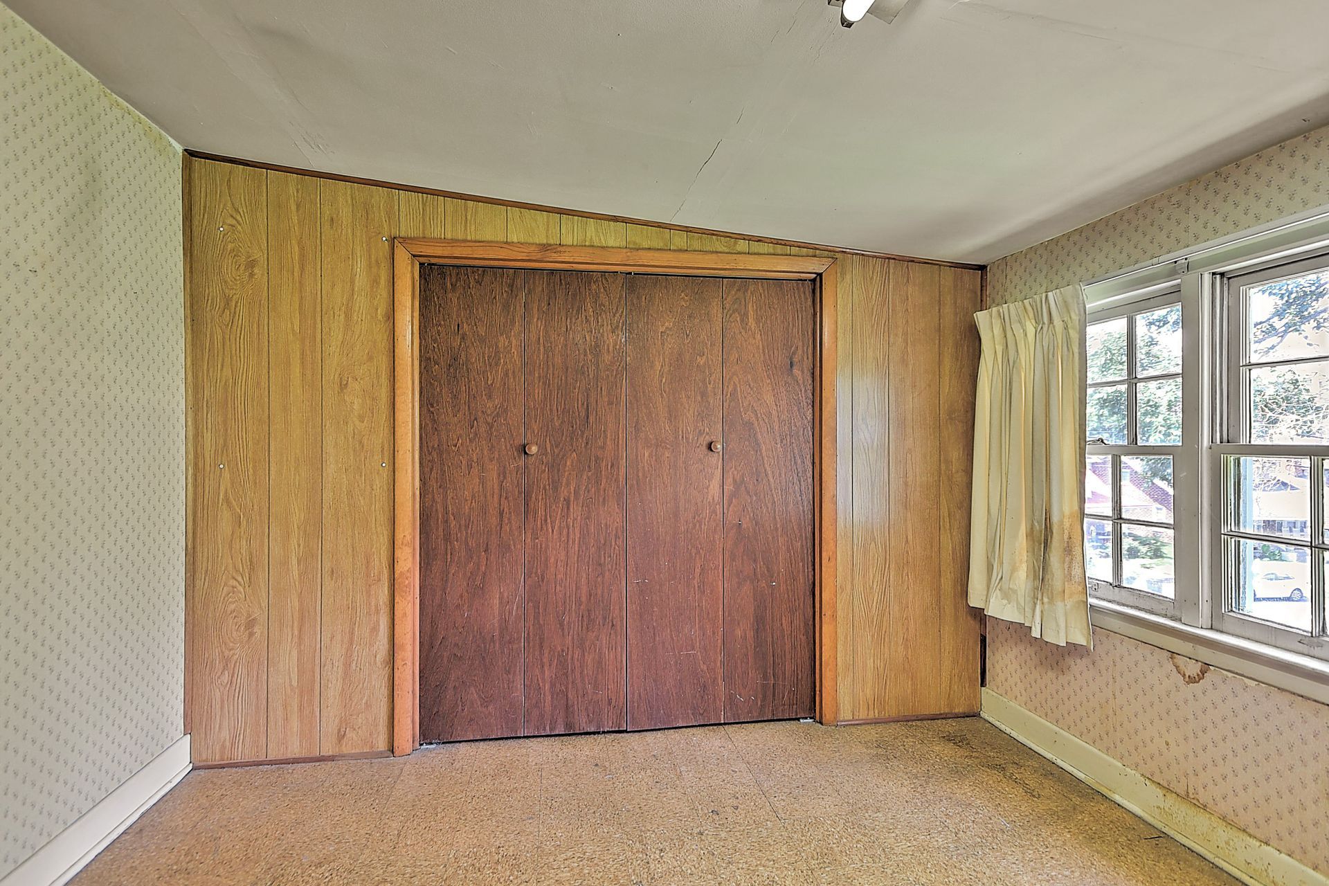 Empty room with wood-paneled wall, large closed double doors, and a window with curtains on the right