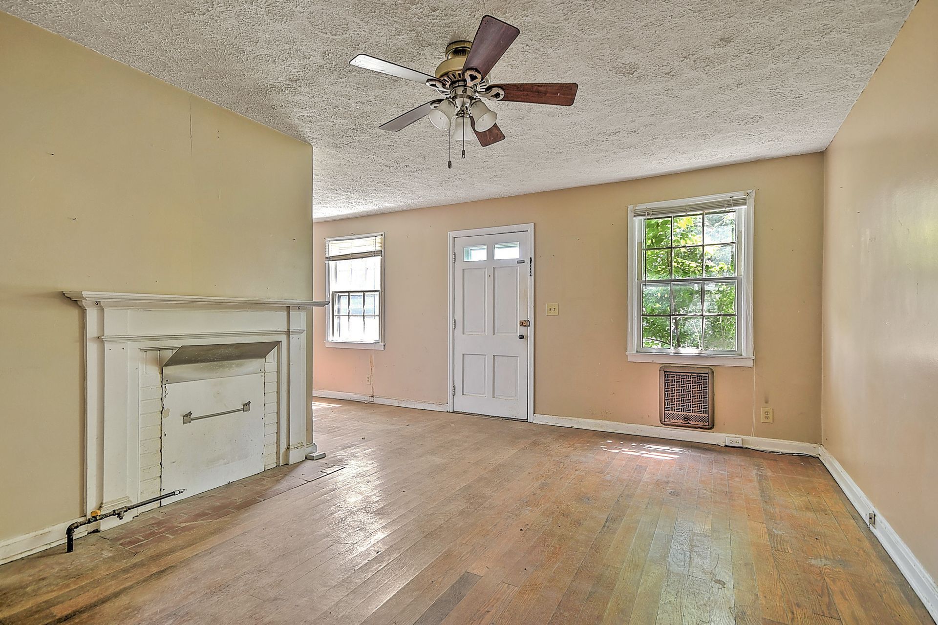 Empty room with beige walls, hardwood floors, fireplace, ceiling fan, and two windows