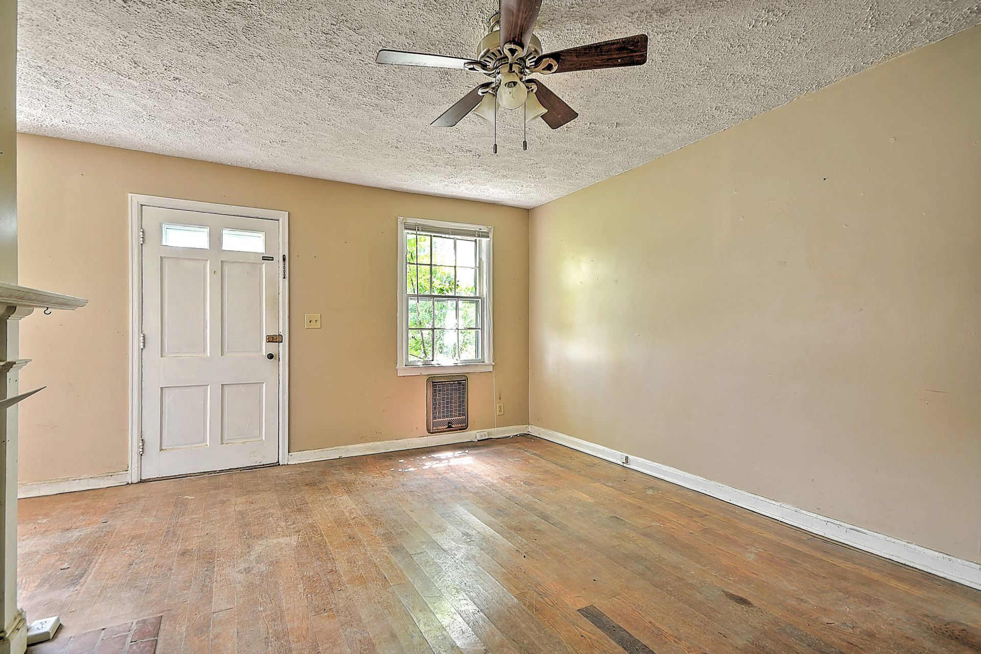 Empty beige room with hardwood floors, white door, window, and ceiling fan