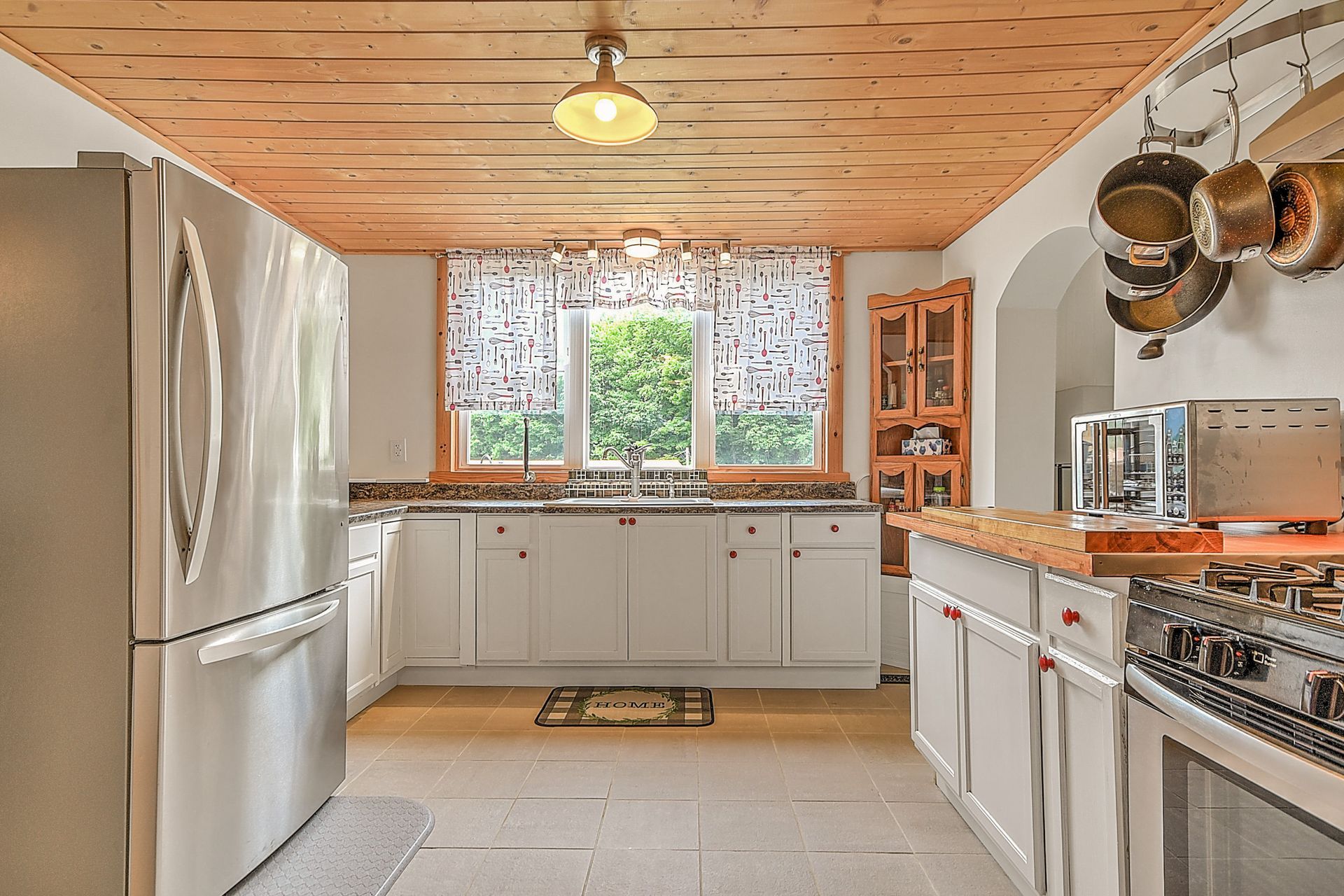 Bright kitchen with white cabinets, stainless fridge, wood ceiling, and a window over the sink.