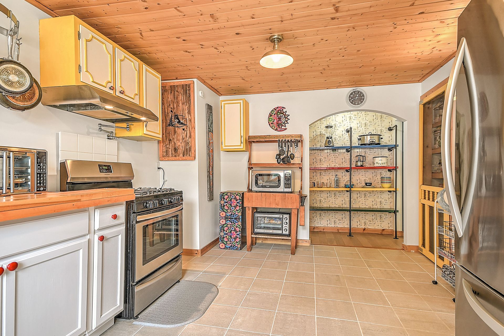 Bright kitchen with white cabinets, wood ceiling, stove, refrigerator, and shelves along the back wall