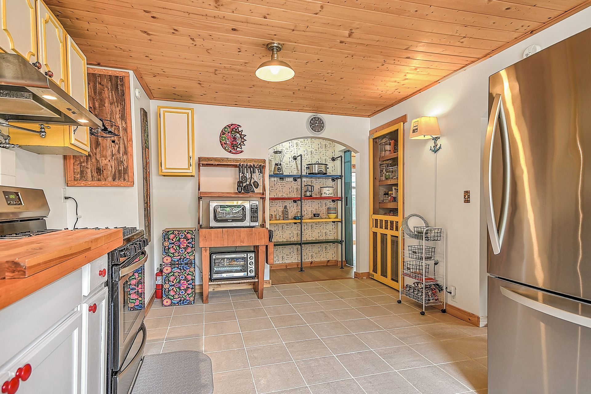Bright kitchen with wood ceiling, stainless fridge, white cabinets, and glass-front hutch in the dining area
