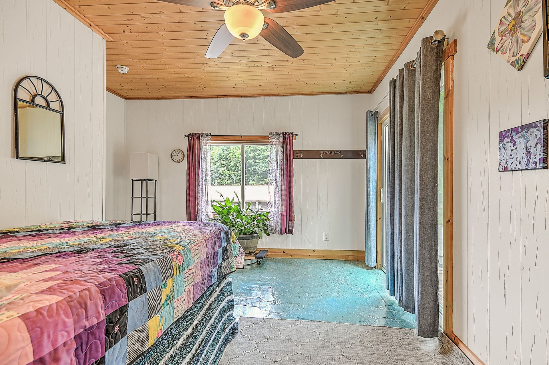 Bright bedroom with twin beds, blue carpet, wood ceiling, ceiling fan, and a large window with curtains