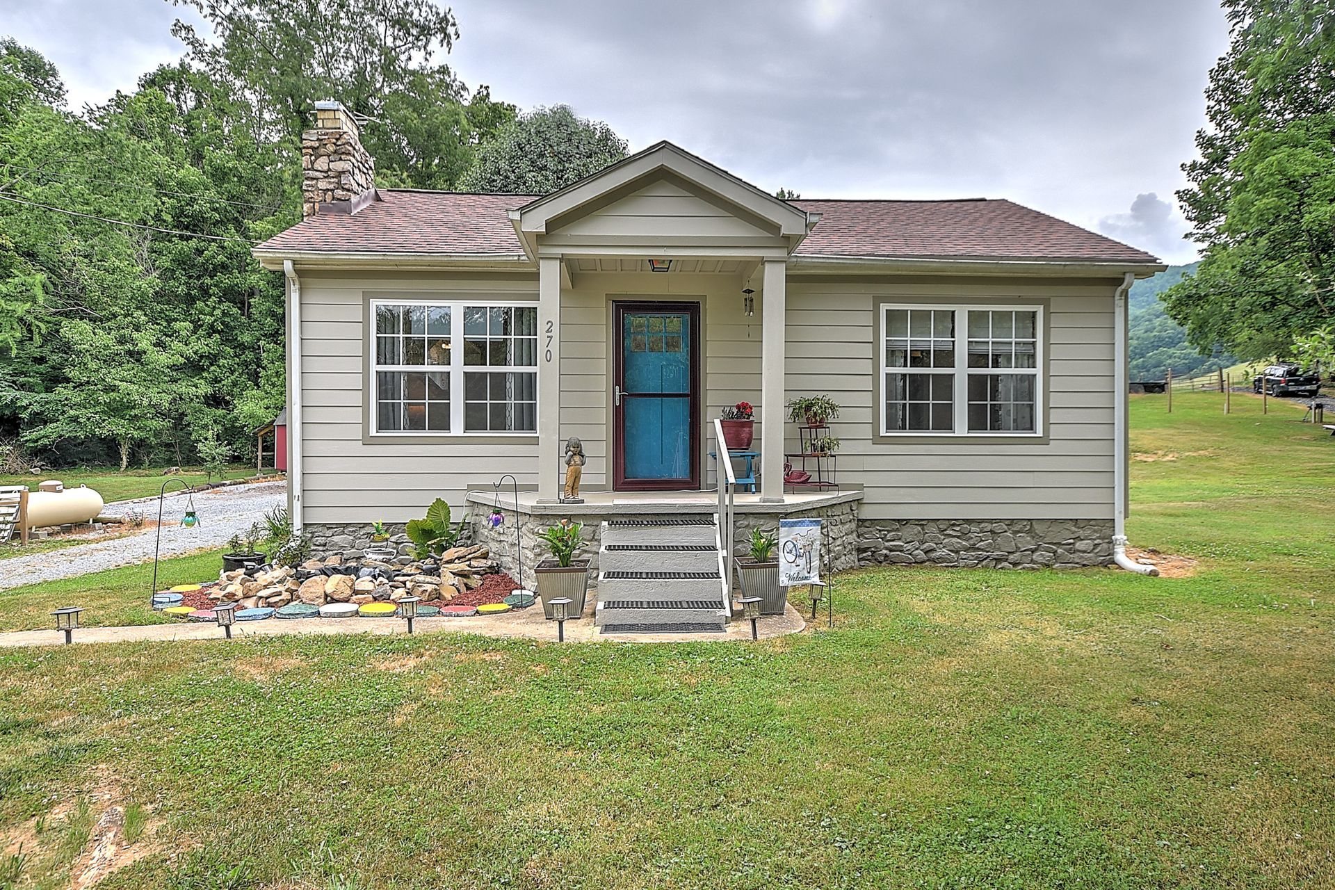 Small gray house with a blue front door, a child on the steps, and a grassy yard.
