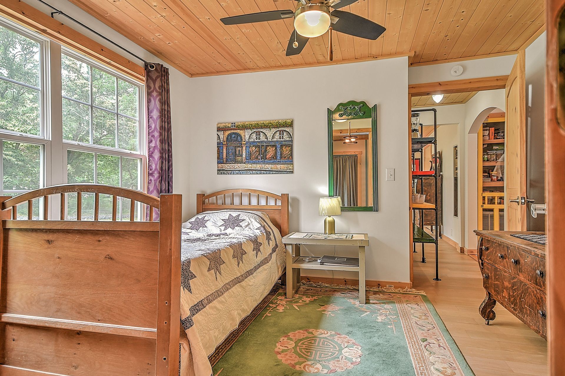 Cozy bedroom with wood ceiling, twin beds, green rug, and large window with forest view