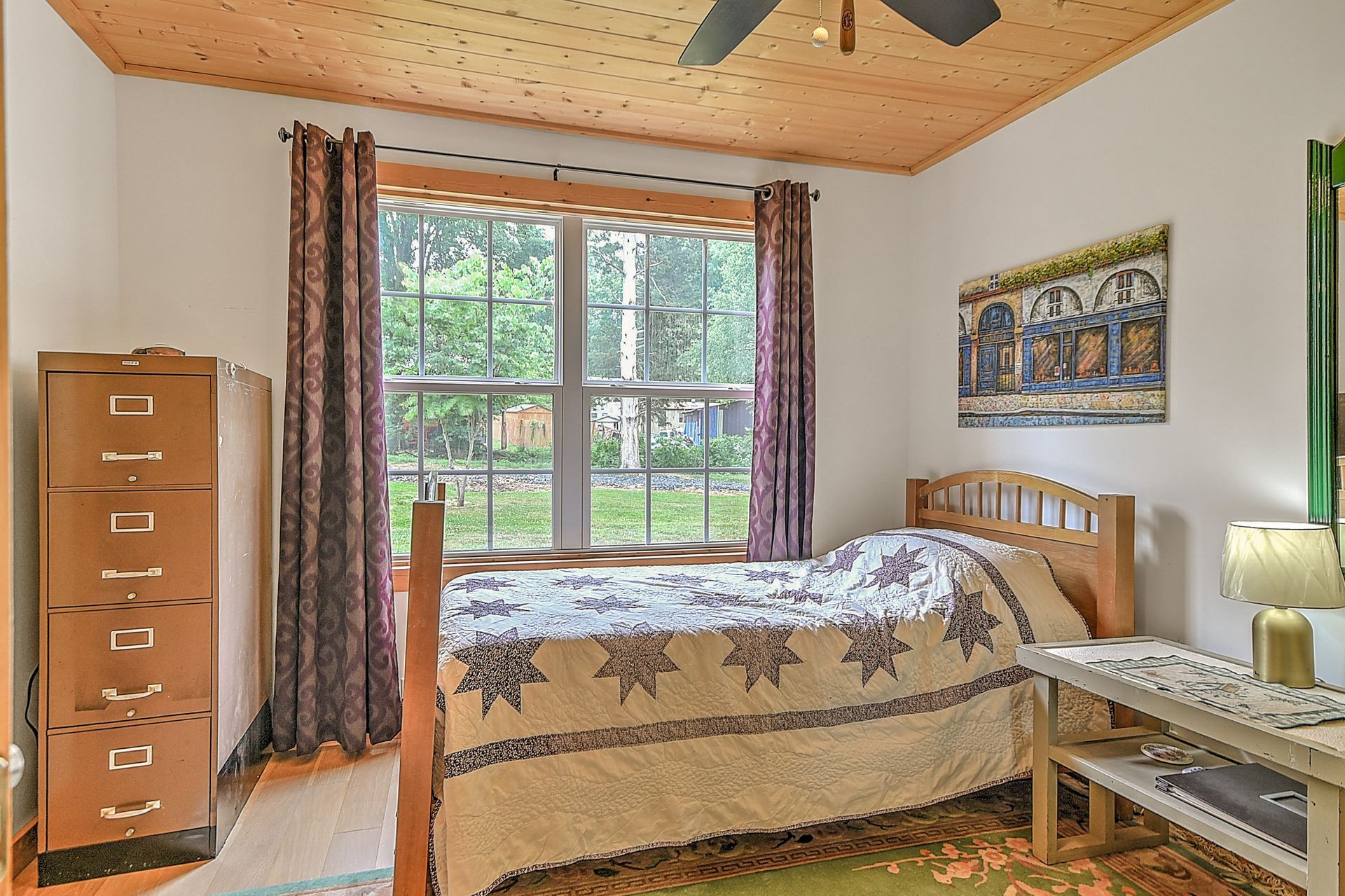 Bedroom with twin bed, large window, wooden dresser, and desk in a bright, cozy room