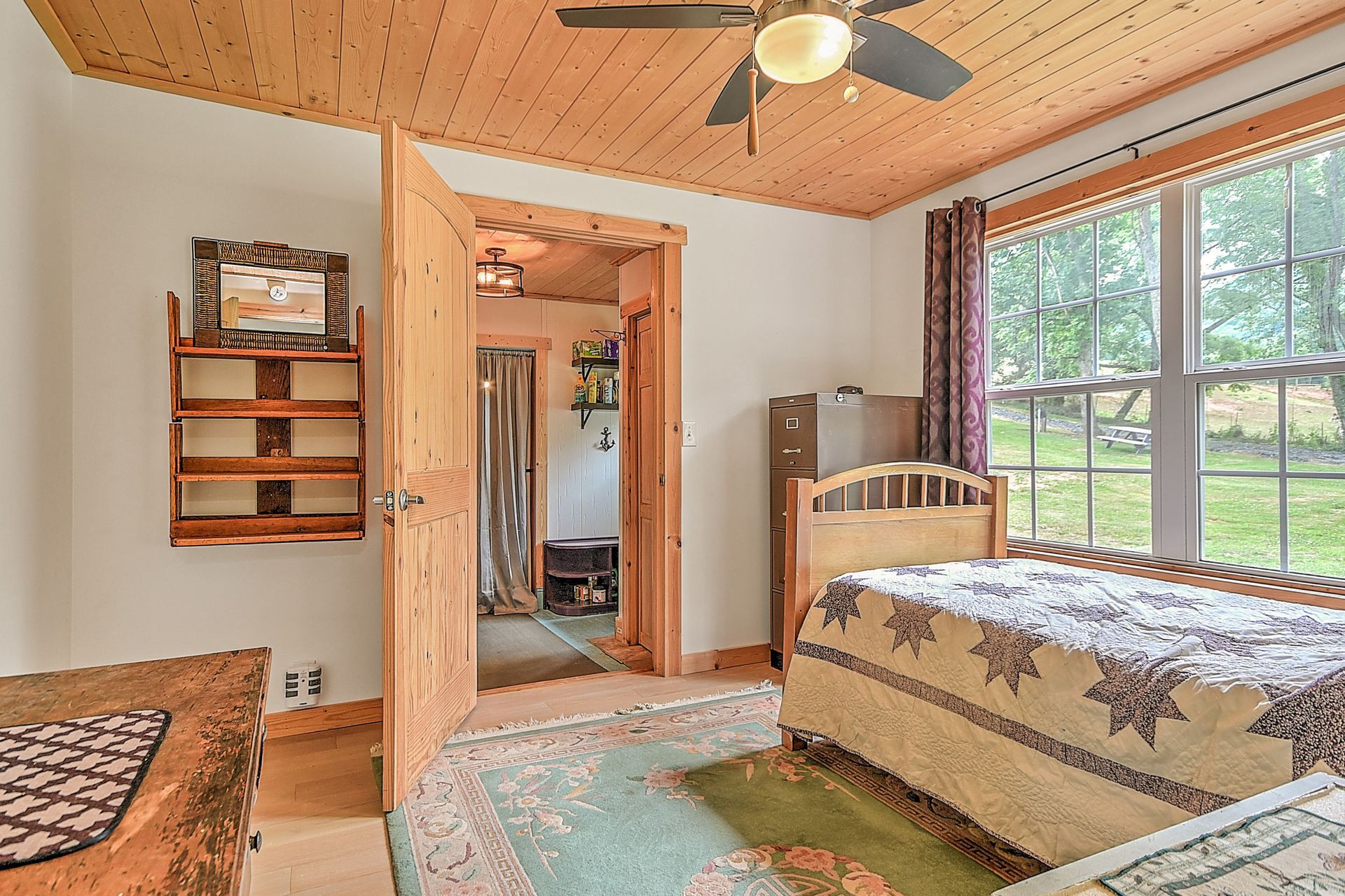 Bedroom with wood ceiling, ceiling fan, bed, window, and open doorway to bathroom