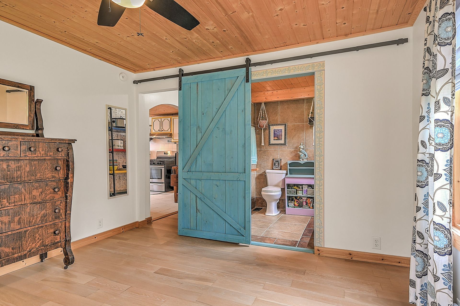 Bright room with a turquoise sliding barn door, wood ceiling, dresser, and curtain-framed doorway
