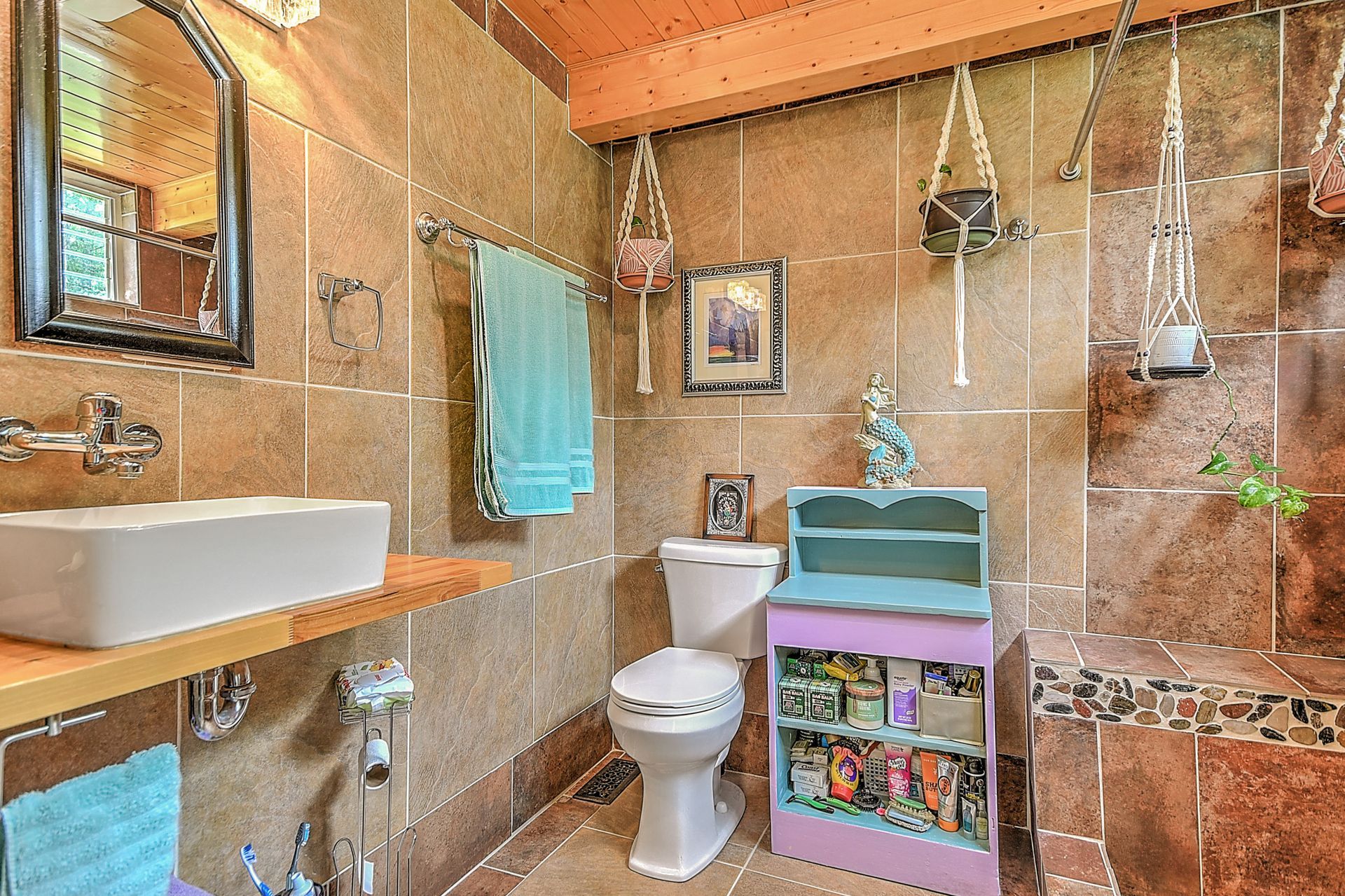 Small tiled bathroom with sink, toilet, shower, turquoise towels, and hanging plants