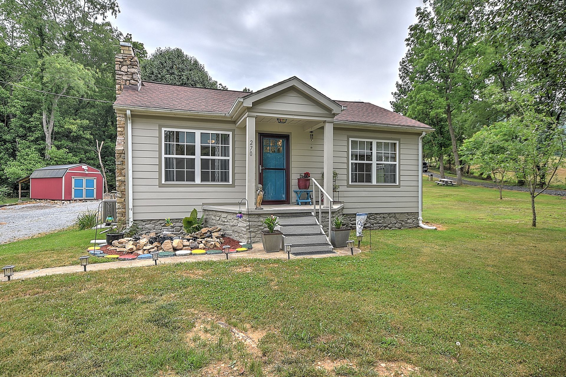 Small beige house with blue front door, stone steps, and a large grassy yard with trees.