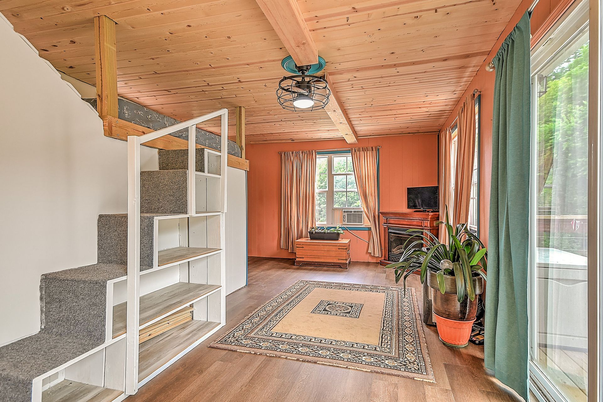 Bright living room with wood ceiling, staircase, rug, plants, and sliding glass doors to a patio