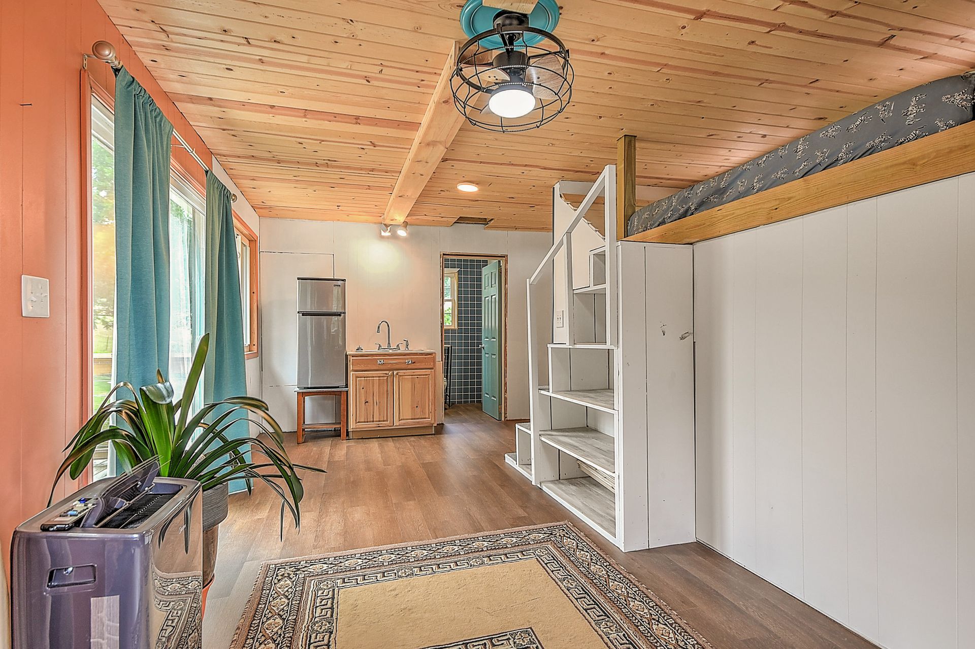 Bright sunroom with wood ceiling, white shelving, plants, rug, and a desk near large windows