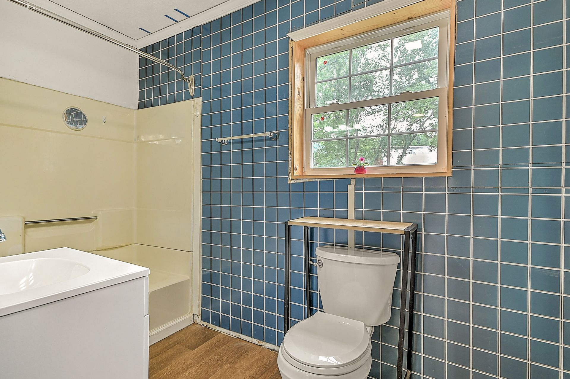 Blue-tiled bathroom with toilet under a window, beige tub wall, and white vanity edge