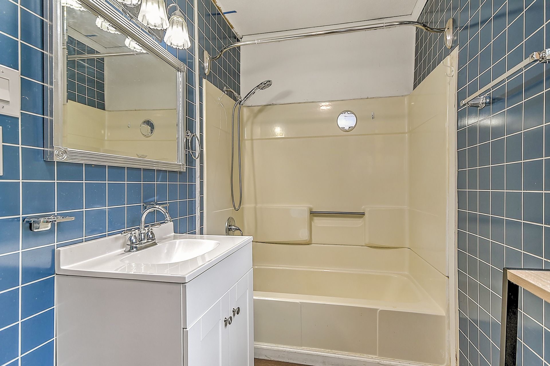 Blue-tiled bathroom with vanity, mirror, and beige shower/tub area