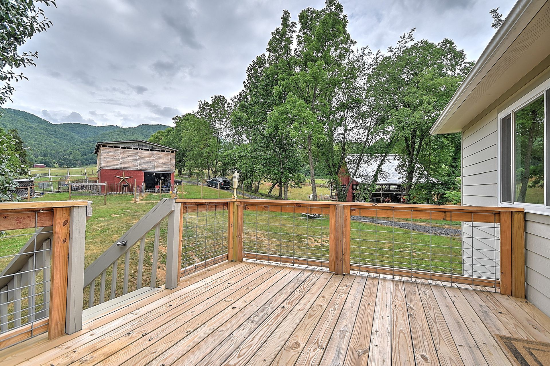Wooden deck overlooking a grassy yard, old red barn, and trees under a cloudy sky