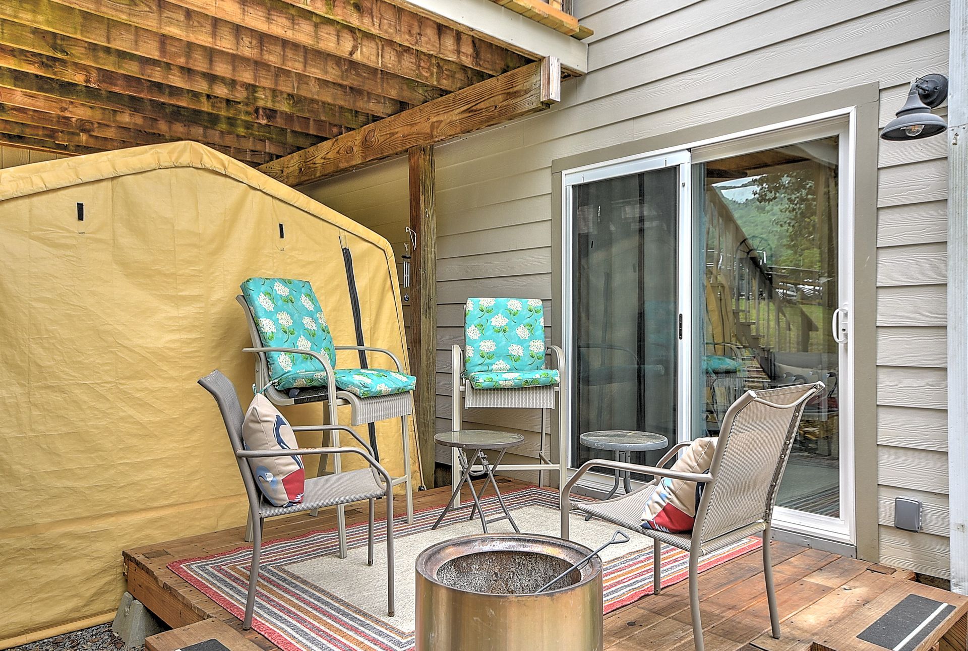 Patio seating area with chairs, fire pit, striped rug, and sliding glass doors beside a tan canopy tent