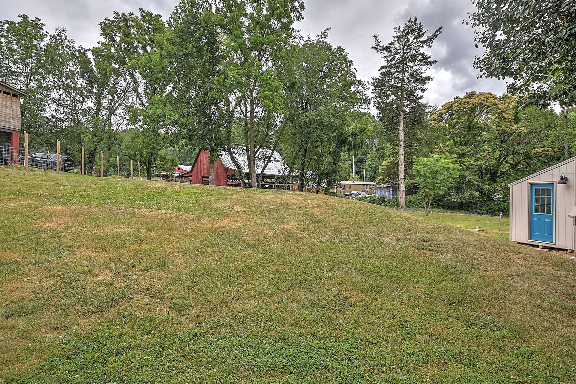 Grassy yard with trees, a red playground structure, and a small shed under a cloudy sky
