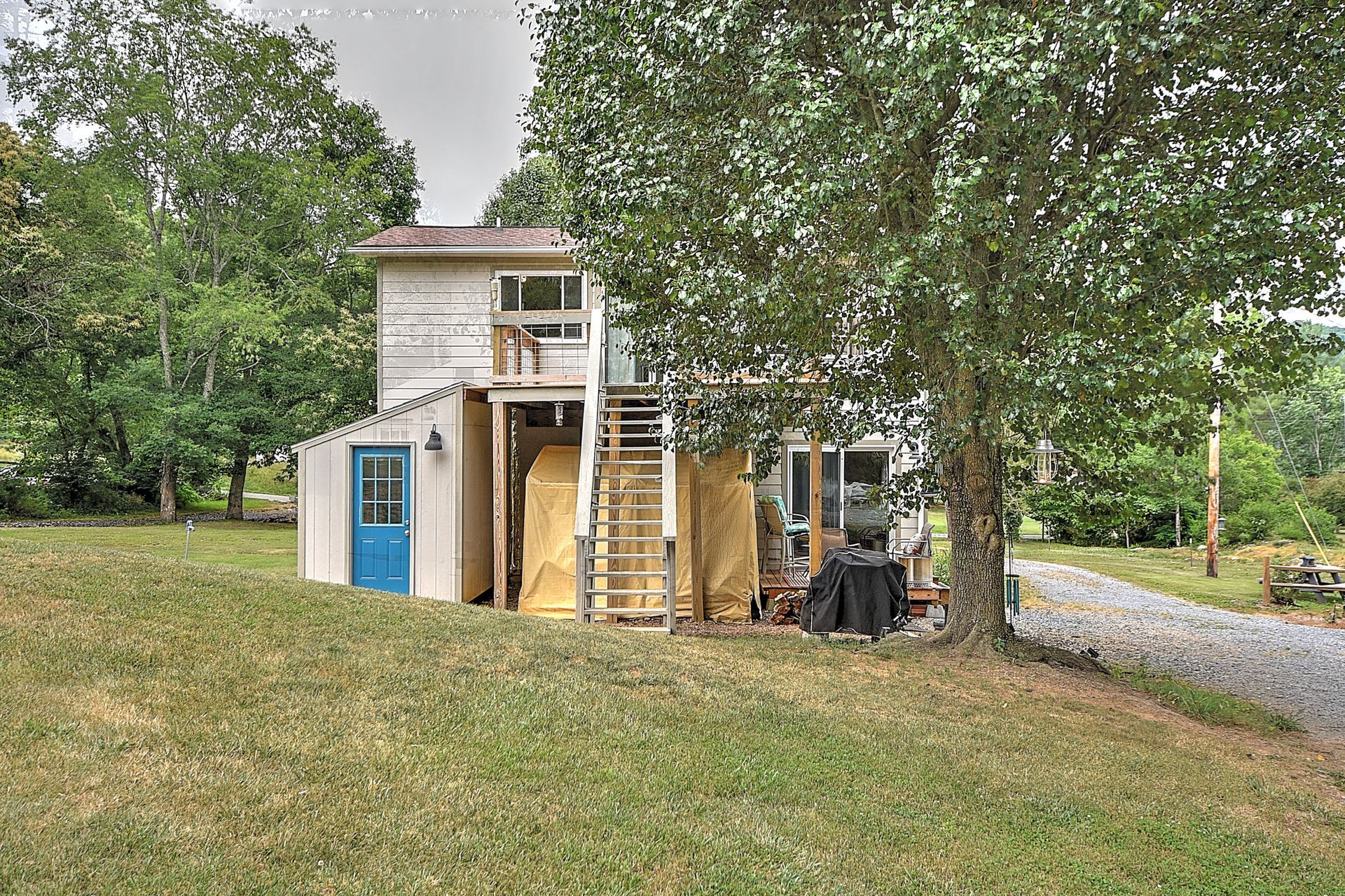 Small wooden playhouse with blue door in a grassy yard, surrounded by trees and a gravel path.