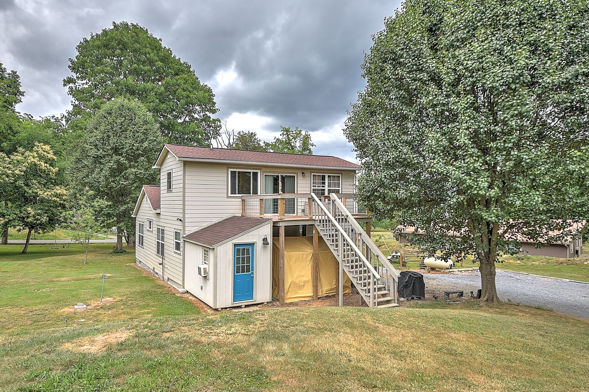 Two-story house with an external staircase, blue door, and large trees in a grassy yard