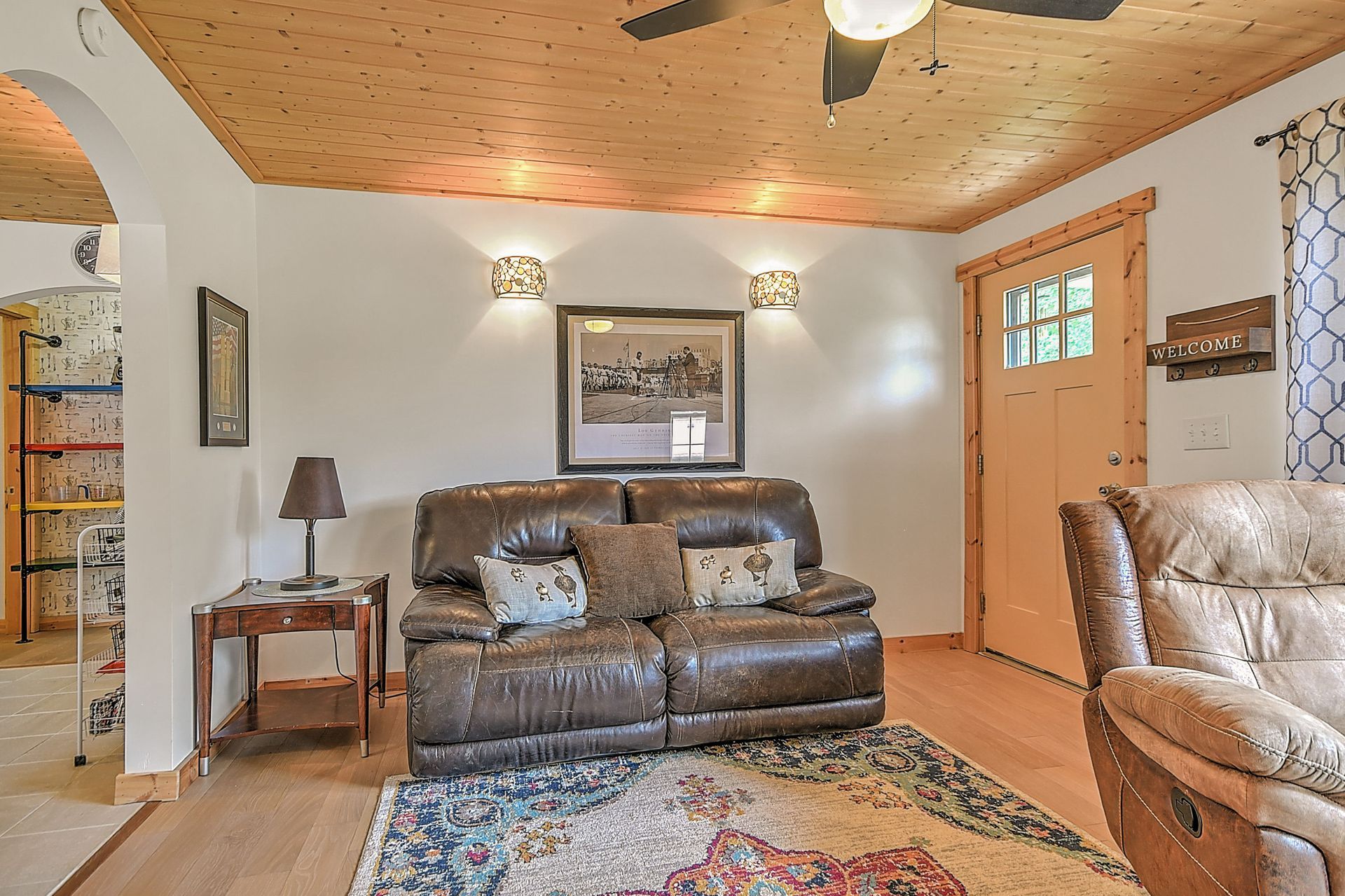 Living room with brown leather sofa, patterned rug, wood ceiling, and front door with window panels
