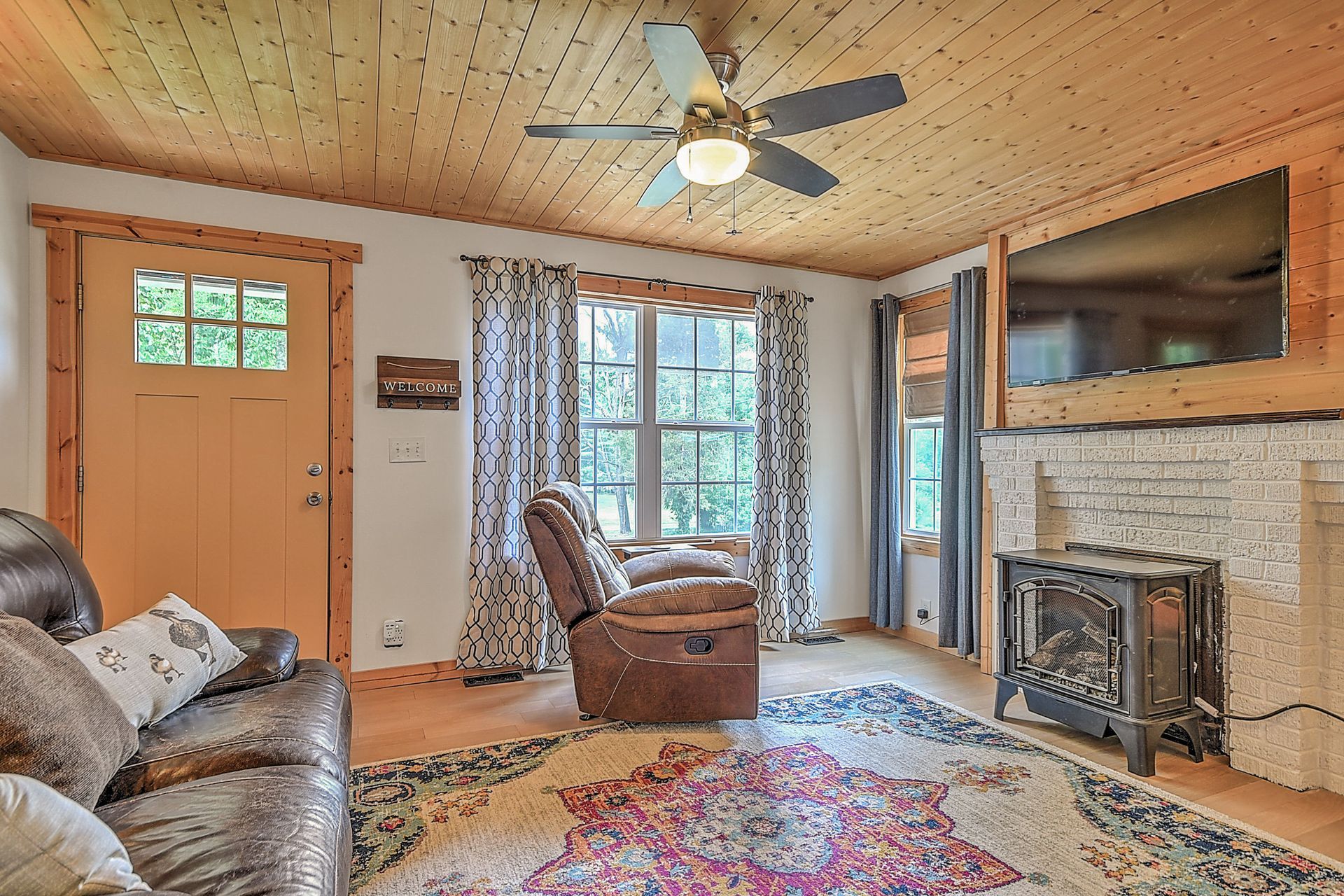 Cozy living room with stone fireplace, recliner, patterned rug, orange door, and large window.