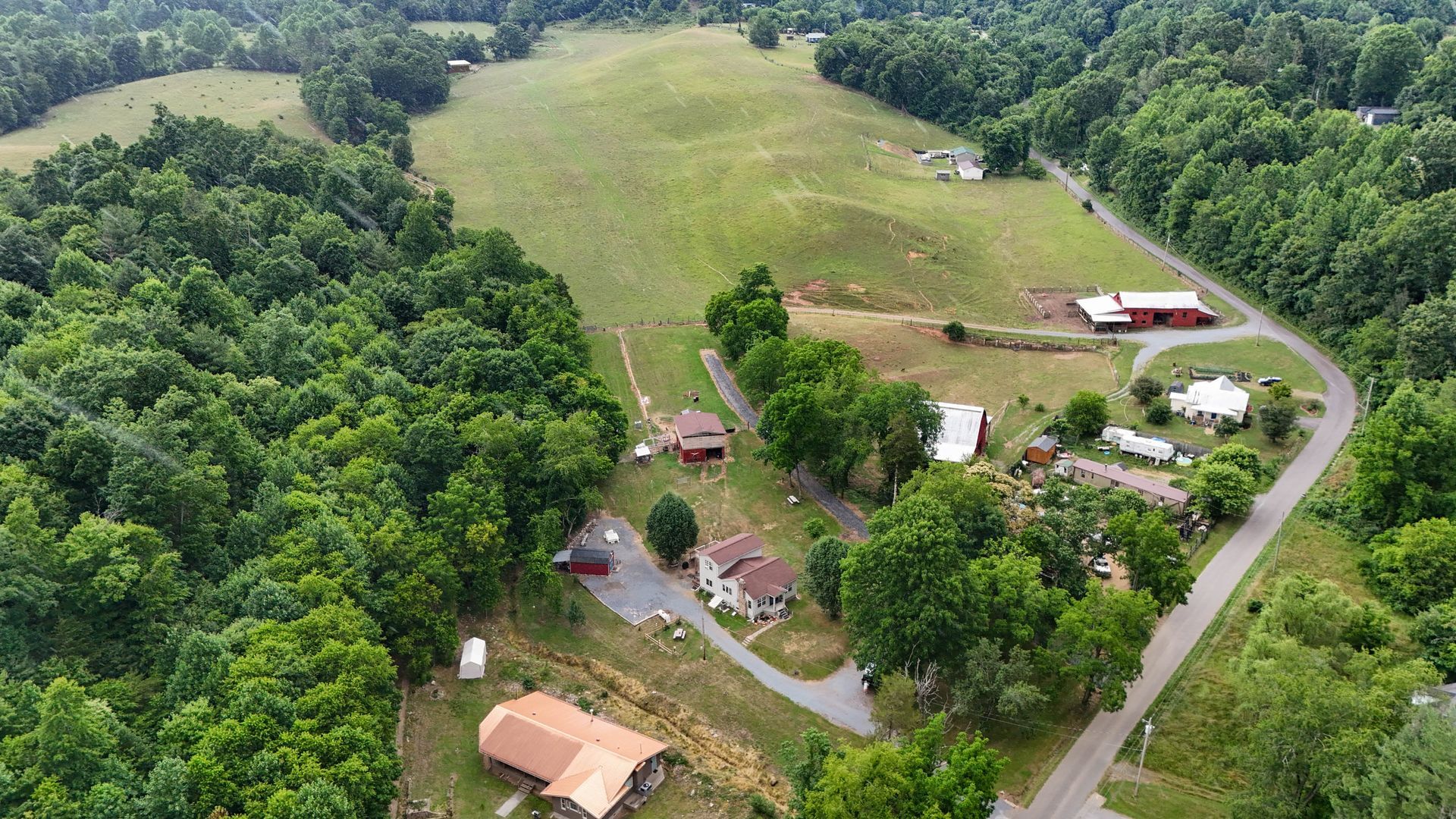 Aerial view of a rural farmstead with fields, trees, winding road, and scattered houses and barns.