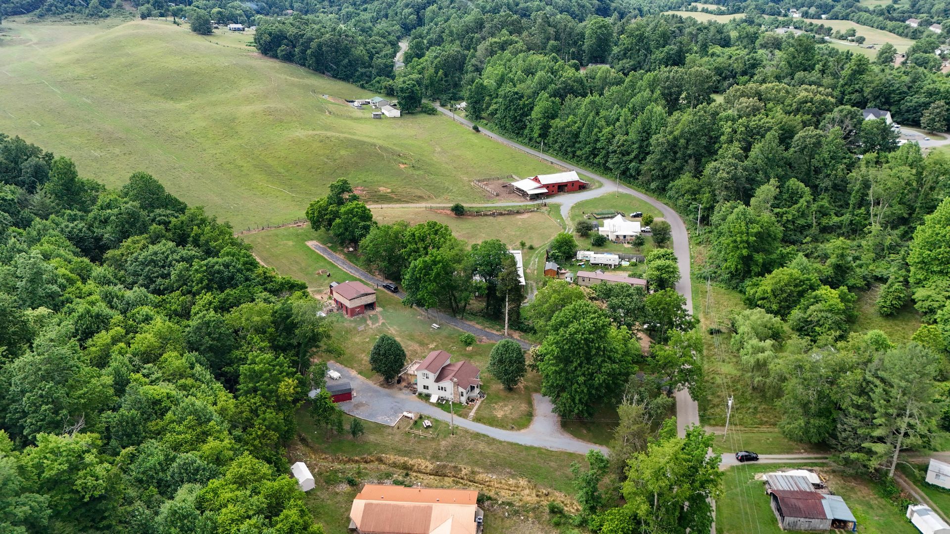 Aerial view of a rural farmstead with green fields, trees, and scattered houses along a winding road.