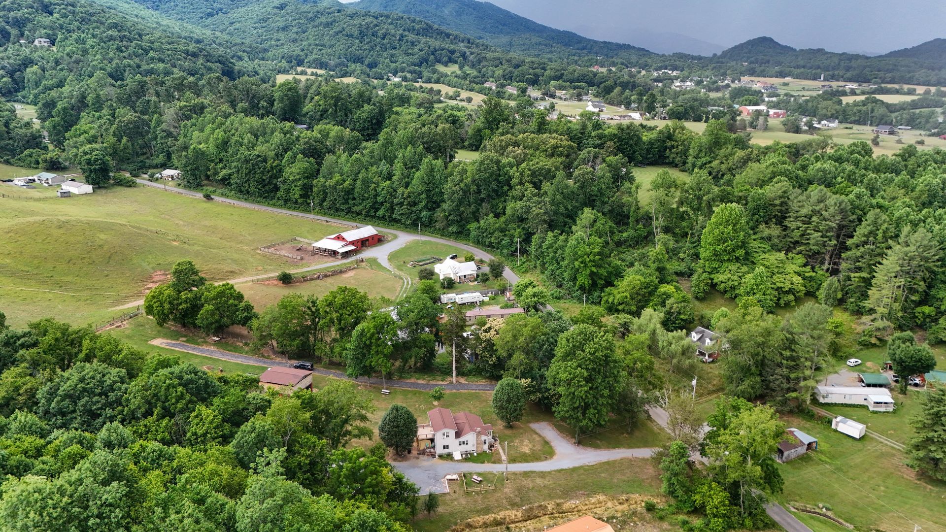 Aerial view of a rural green valley with scattered houses, fields, and forested hills.