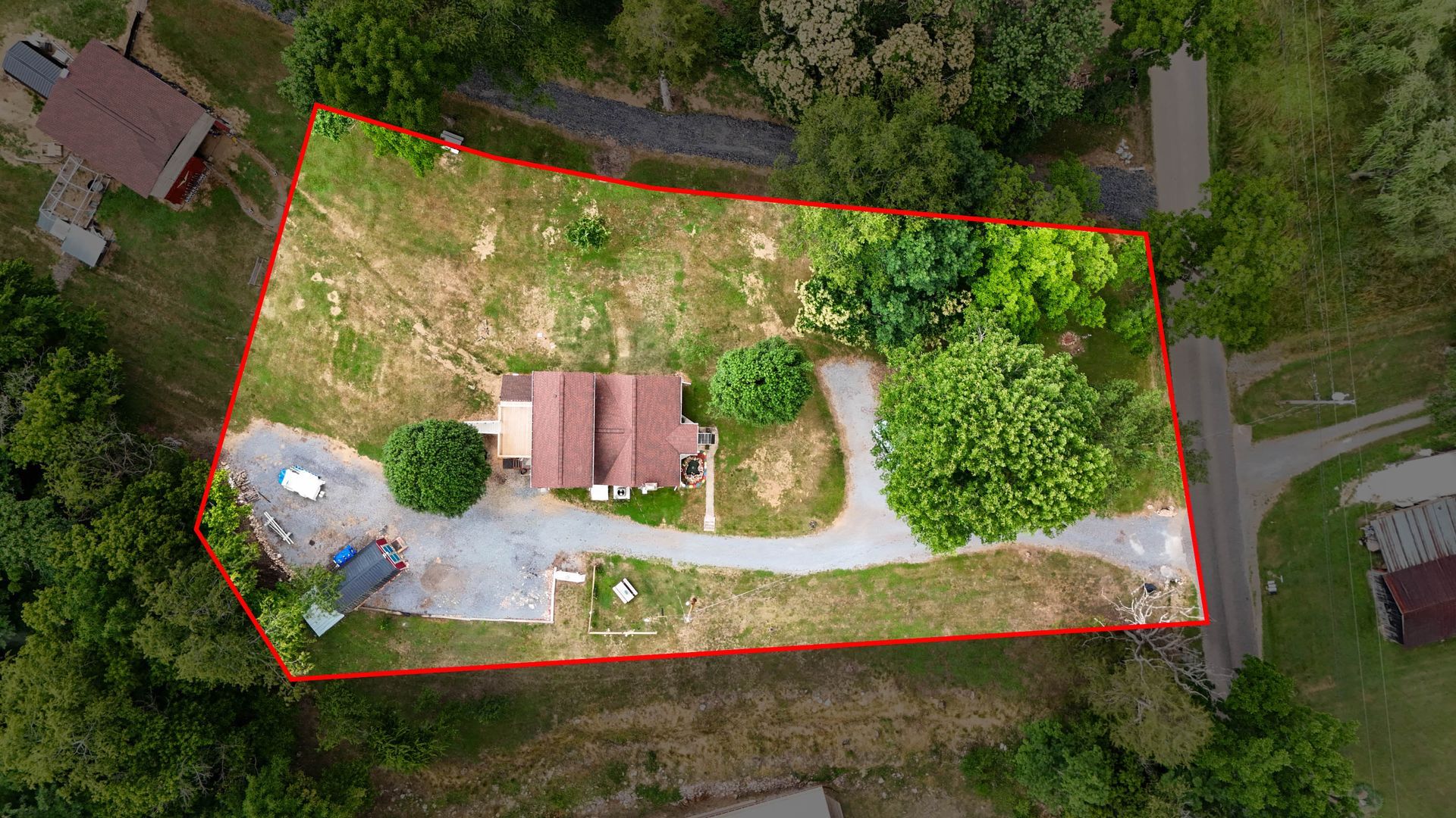 Aerial view of a house with a driveway and trees, outlined by a red property boundary.
