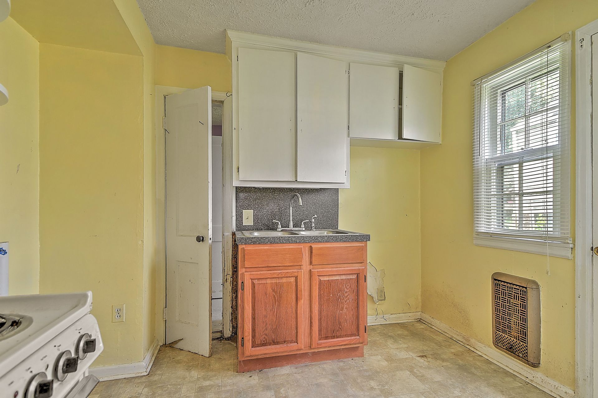 Small empty kitchen with yellow walls, white cabinets, wood base cabinet, and a window with blinds.