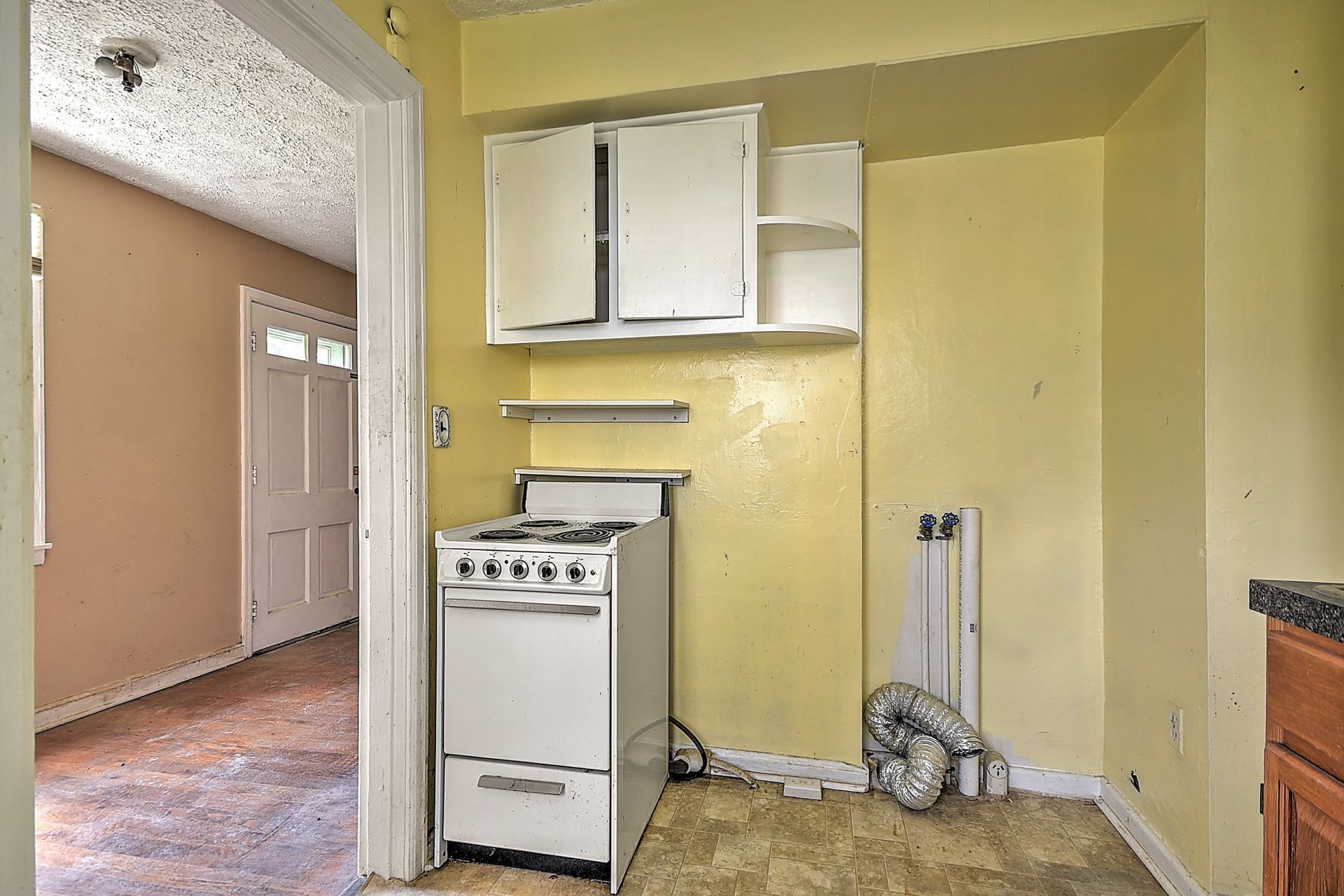 Small yellow kitchen with white stove, wall cabinets, and a doorway to a hall with a front door.