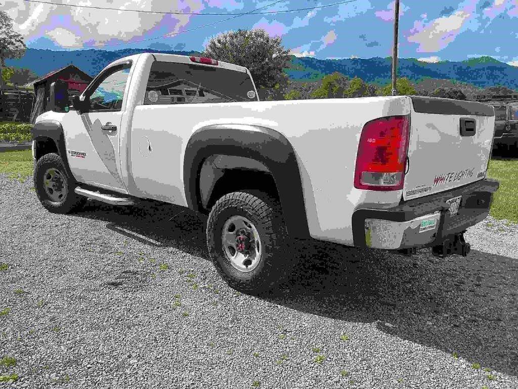 White pickup truck parked on gravel beside a building, with mountains and blue sky in the background
