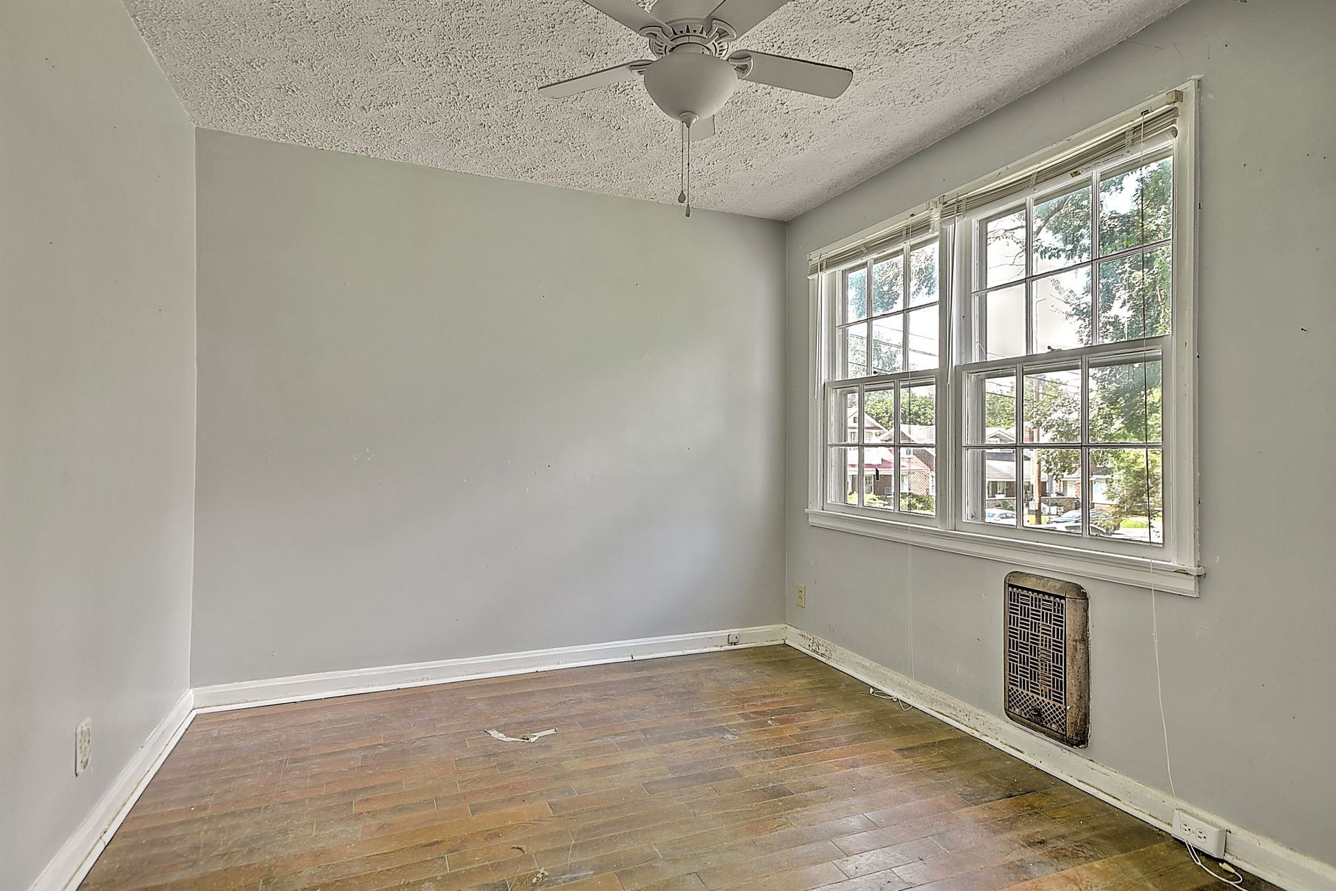 Empty white room with hardwood floor, large window, and textured ceiling.