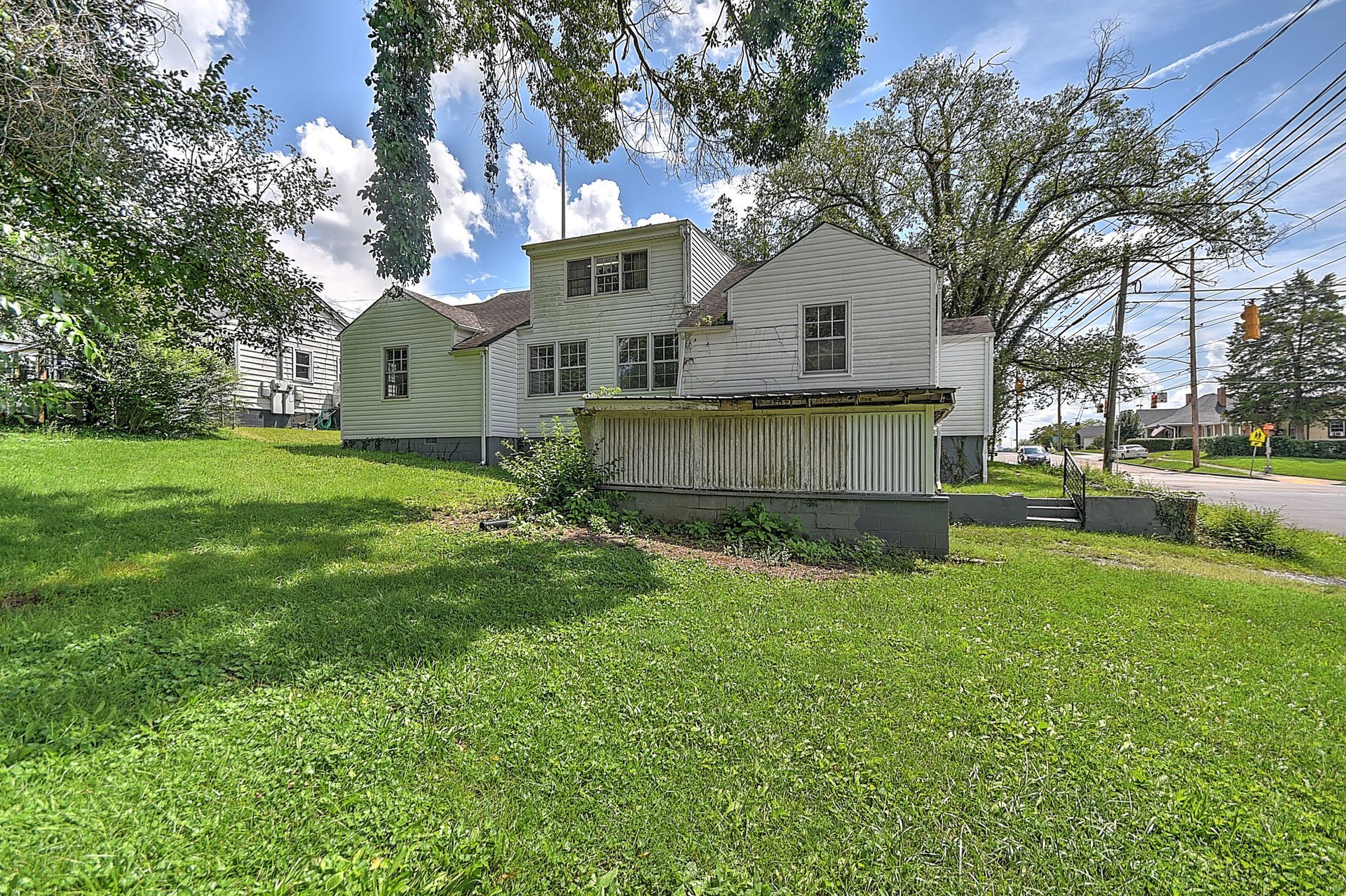 Old white house with a porch on a grassy lot under trees and a blue sky
