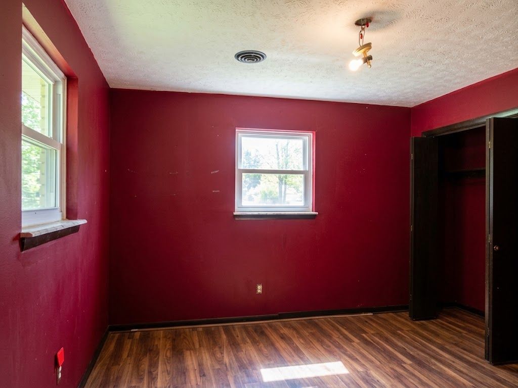 Empty room with burgundy walls, wood floor, two windows, and an open closet.